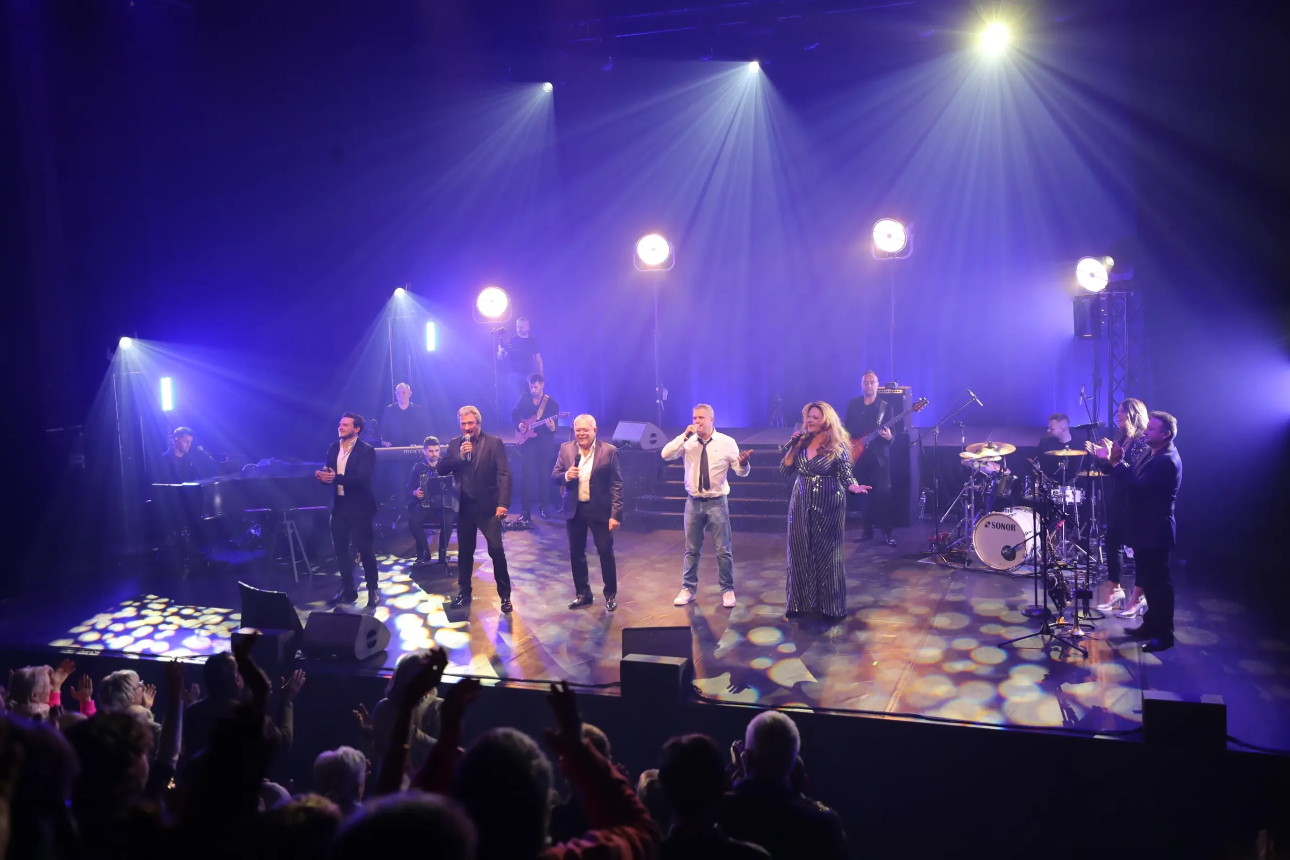 tous les sosies vocaux regroupés sur scène chantent devant le public qui applaudit